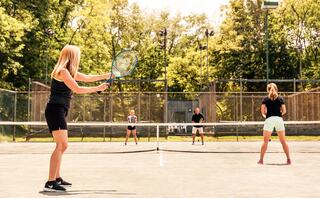 A group of four people plays tennis on a sunny court, with two players at the net and two preparing for a rally in the background.