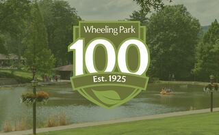 A modern white building features arched windows, a decorative round element, and steps leading up, surrounded by trees and benches.