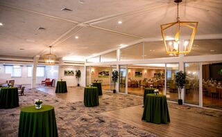 A spacious, elegantly designed event space featuring green tablecloths, modern lighting, and large windows overlooking a dining area.