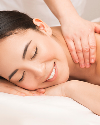 A relaxed woman smiles contentedly as she receives a soothing massage, eyes closed in blissful tranquility.