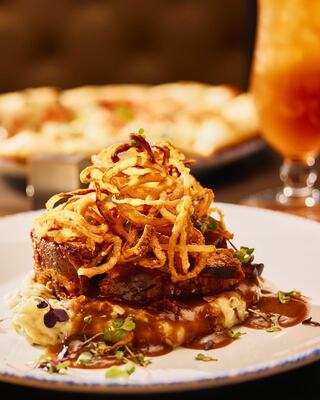 Succulent meatloaf topped with crispy onion rings, served over creamy mashed potatoes and gravy, with a refreshing drink in the background.