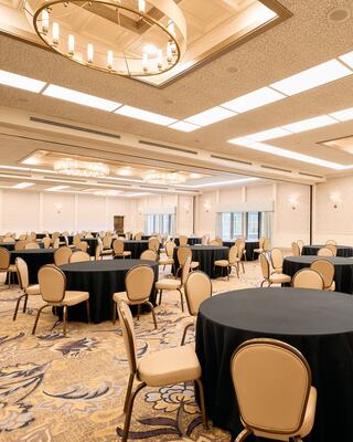 A spacious banquet hall with round tables covered in black cloth and elegant chairs, complemented by stylish lighting and decor.