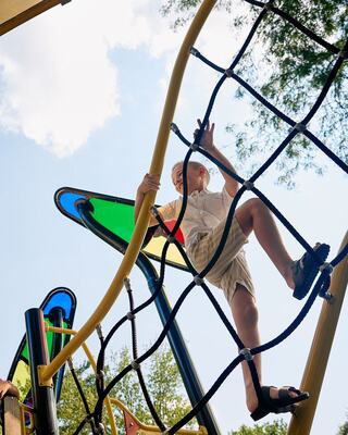 A child climbs a colorful playground structure under a bright sky, showcasing excitement and adventure.