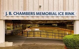 A sign displays "J. B. Chambers Memorial Ice Rink" above an entrance, leading to a visible indoor ice rink and surrounding greenery.