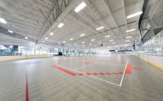 A spacious indoor arena features a smooth, tiled surface marked for a sport, with clear walls and overhead lighting. Bright and inviting atmosphere.