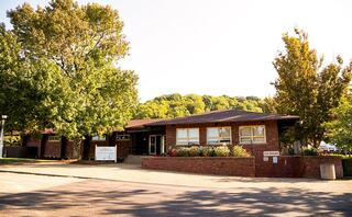 A modern brick building surrounded by trees, featuring a landscaped entrance and clear blue skies, creating a welcoming atmosphere.
