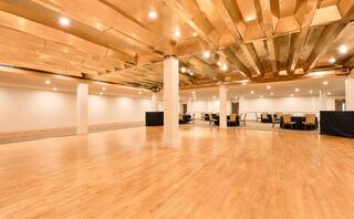 A spacious hall featuring hardwood floors, bright lights, and a ceiling with decorative beams, ideal for events and gatherings.