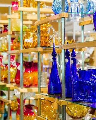 A vibrant display of colorful glassware in various shapes and sizes, arranged on wooden shelves that highlight their beauty.