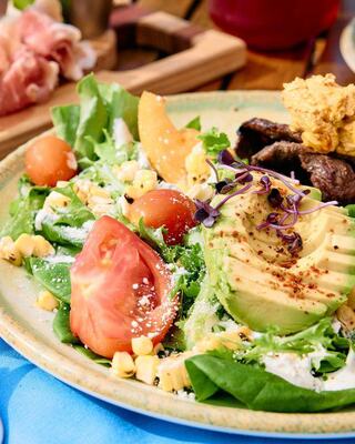 A vibrant salad featuring fresh greens, cherry tomatoes, avocado, corn, and a dollop of hummus, garnished with microgreens.