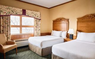 Cozy hotel room featuring two double beds, a comfortable chair, and large windows allowing natural light to fill the space.
