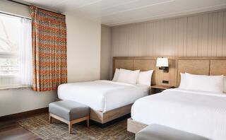 A stylish hotel room features two cozy beds, warm wood accents, and colorful curtains, creating a welcoming ambiance.