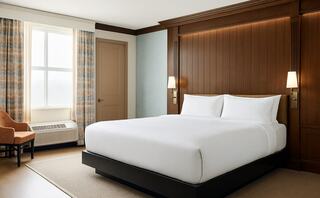 A cozy room features dark wooden furniture, including a wardrobe and dresser, with a small round table and seating area by a window.