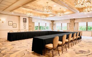 A spacious meeting room features a large rectangular table with black cloth, surrounded by beige chairs and illuminated by elegant chandeliers.