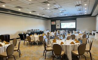 A banquet room features neatly arranged tables with white tablecloths and golden napkins, set for an event or gathering.