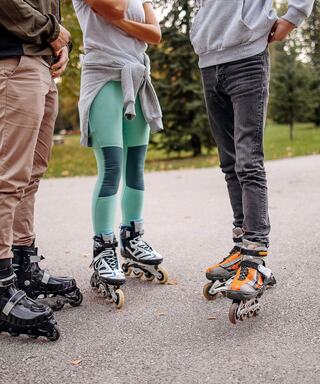 Three individuals in casual attire are standing on a pathway, each wearing roller skates, ready to enjoy some outdoor skating.