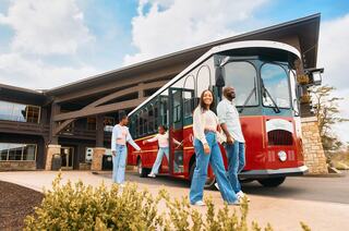 A joyful family enjoys a nature walk, with a child perched on the father's shoulders while the mother walks alongside, surrounded by trees.