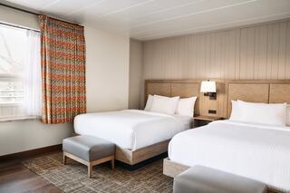 A cozy bedroom features two beds, a stylish rug, and colorful curtains, creating a warm and inviting atmosphere.