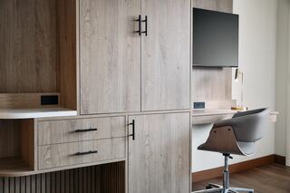 A modern workspace features wood cabinetry, a sleek chair, and a wall-mounted TV, creating a minimalist and functional design.