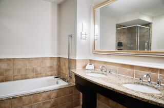 A stylish bathroom featuring a tub, double sinks with granite counters, modern fixtures, and a large mirror. Soft lighting and elegant tiles complete the look.