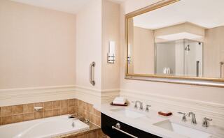 A stylish bathroom features a large soaking tub, double sinks with sleek fixtures, and a spacious shower, all in soft, neutral tones.