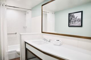 A modern bathroom features sleek white surfaces, a large mirror, a framed photo, and a shower with curtains, creating a clean aesthetic.