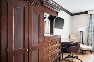 A cozy room featuring dark wood furniture, a stylish dresser, a mounted TV, and a comfortable seating area with patterned curtains.