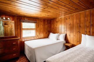 Cozy wooden bedroom featuring two twin beds, a dresser, and a mirror, with warm tones and a classic rustic feel.