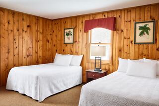 Cozy room featuring wooden walls, two beds, a bedside table with a lamp, and botanical artwork adding a touch of nature.