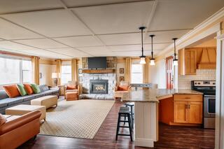 A cozy living space featuring a stone fireplace, a comfortable sofa with colorful cushions, and an open kitchen area with wooden accents.