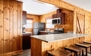 A cozy kitchen features wooden paneling, modern appliances, and a granite countertop, with bar stools inviting casual dining.