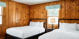 A cozy room features two beds, wooden walls, and natural light from windows, creating a warm and inviting atmosphere.