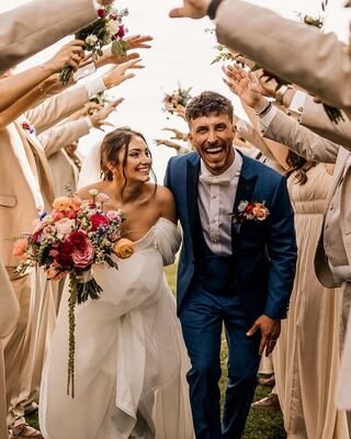A joyful couple celebrates their wedding, surrounded by smiling friends. The bride holds a vibrant bouquet, and both radiate happiness.
