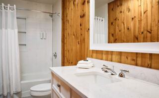 A modern bathroom featuring a wood-paneled wall, white cabinetry, a marble countertop, and a shower with a glass door and curtain. Clean and stylish.