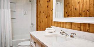 A stylish bathroom featuring a light marble countertop, wooden wall accents, a shower area, and neatly arranged towels.