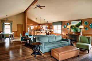 A spacious living area features a green couch, wooden floors, and vibrant decor, seamlessly connecting to a dining space and kitchen.