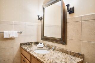 A modern bathroom features a granite countertop, a sink, a decorative mirror, and neatly arranged towels on a rack. Soft lighting enhances the space.