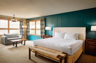 A cozy room features a large bed, a comfy couch, wooden furniture, and windowed walls, creating a warm and inviting atmosphere.