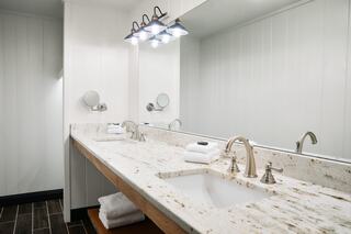 A modern bathroom features a spacious granite countertop with dual sinks, stylish fixtures, and soft lighting, complemented by neatly arranged towels.