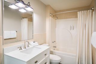 A clean, modern bathroom featuring a white vanity with a mirror, tub and shower combo, and plush towels neatly arranged.