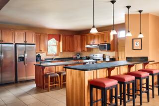 Spacious kitchen featuring wooden cabinets, black countertops, a large island, and bar stools, complemented by pendant lighting.