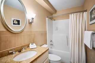 A modern bathroom featuring a round mirror, granite countertop, shower with curtain, and stylish light fixtures. Clean and well-lit space.