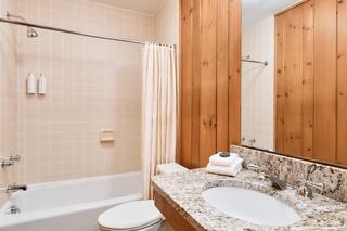 A cozy bathroom featuring a tub with a shower, wooden accents, granite countertop, sink, and neatly arranged toiletries.