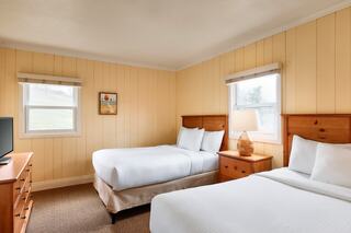 Cozy room featuring two beds, a dresser, a lamp, and windows with natural light, all set against warm wooden walls.