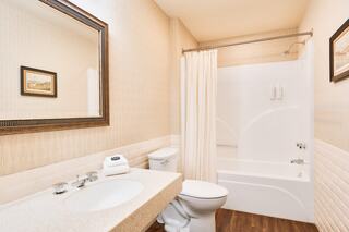 A small, clean bathroom features a sink with a mirror, a toilet, and a shower-tub combo with a curtain, all in neutral tones.
