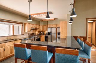 A modern kitchen with wooden cabinetry, granite countertops, and blue upholstered bar stools. Bright lighting enhances the open space.