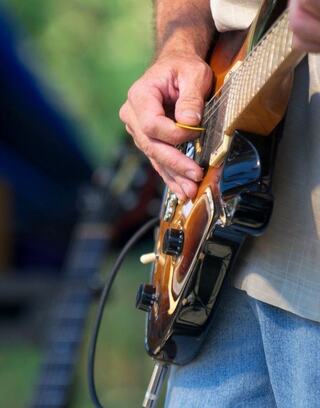 A hand skillfully plays an electric guitar, showcasing intricate finger movements against a blurred outdoor setting.