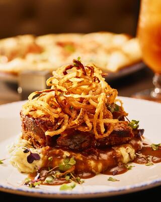 Succulent meatloaf topped with crispy fried onions, served over creamy mashed potatoes and rich gravy, garnished with fresh herbs.