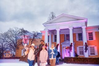 A joyful group of people, including a child holding a teddy bear, admire colorful holiday lights while bundled up in winter clothing.