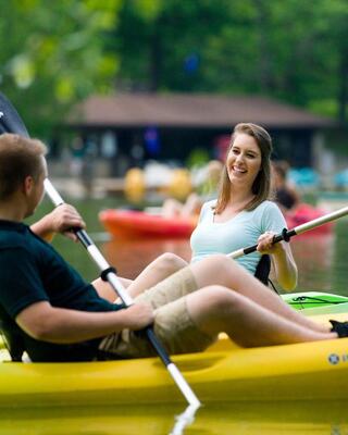 Two children wearing sunglasses play in a blue pool, splashing water and enjoying a sunny day on colorful floaties.