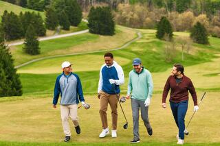 Four friends walk together on a lush golf course, enjoying their time outdoors, dressed in casual golf attire and holding clubs.